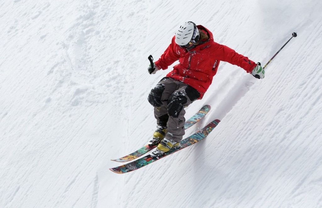 Skifahrer mit roter Jacke und schwarzer hose bei einer rasanten Abfahrt