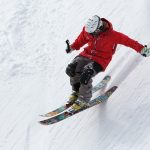 Skifahrer mit roter Jacke und schwarzer hose bei einer rasanten Abfahrt