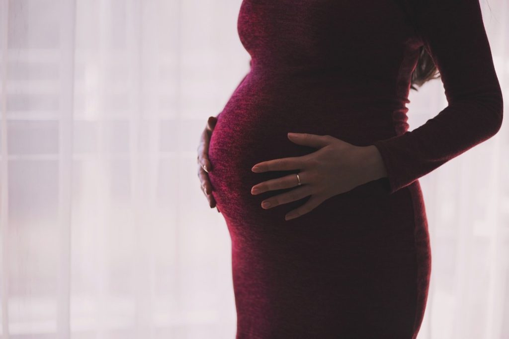 Schwangere Frau in einem roten Kleid die sich mit beiden Händen sanft den Bauch hält