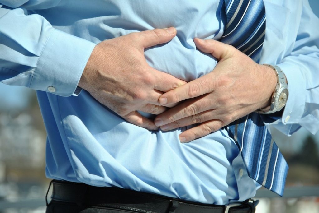 Mann der sich mit beiden Händen krampfhaft den Bauch hält